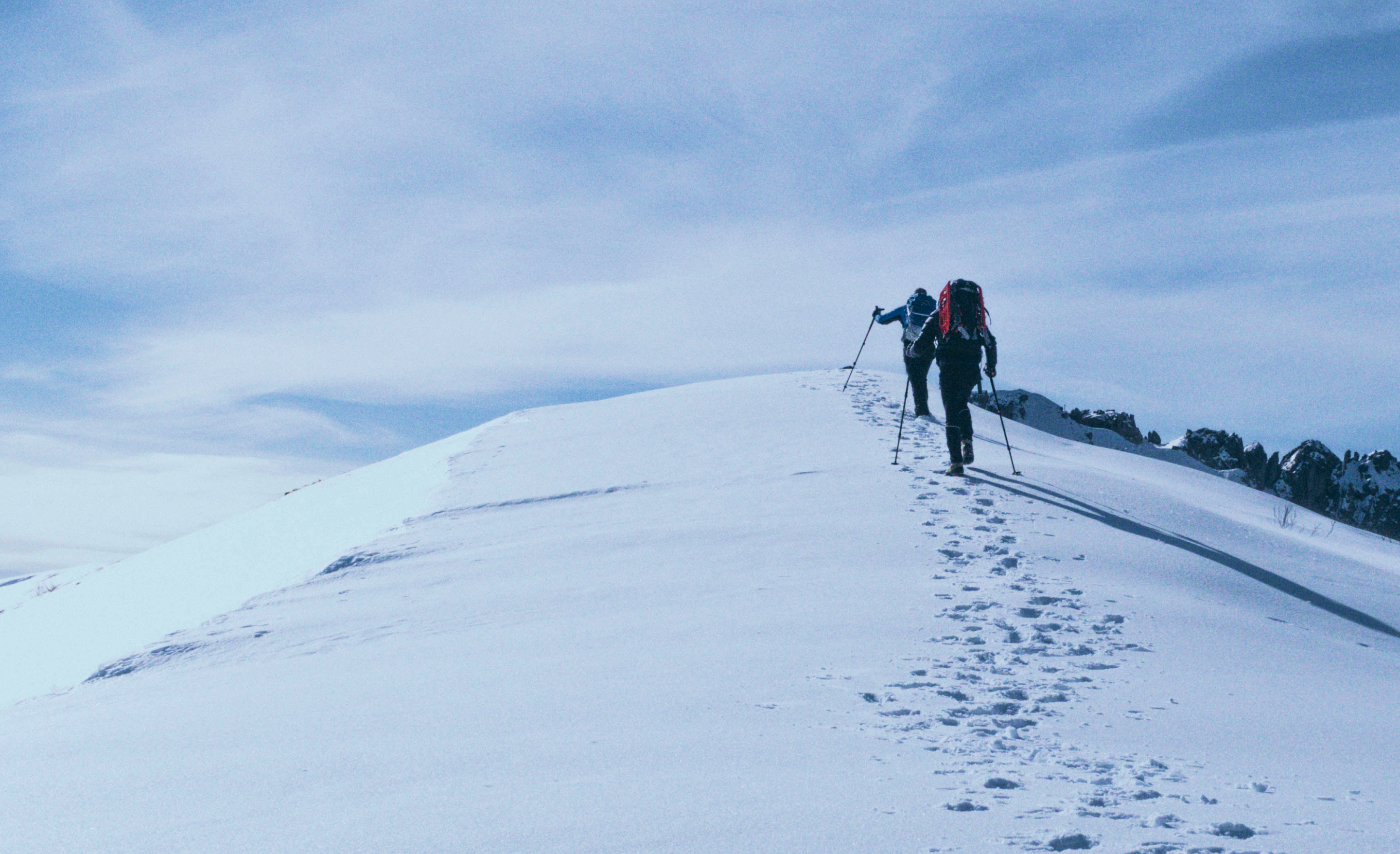 雪山を登るハイカー二人が、トレッキングポールを使用して、雪に覆われた坂を登っている
