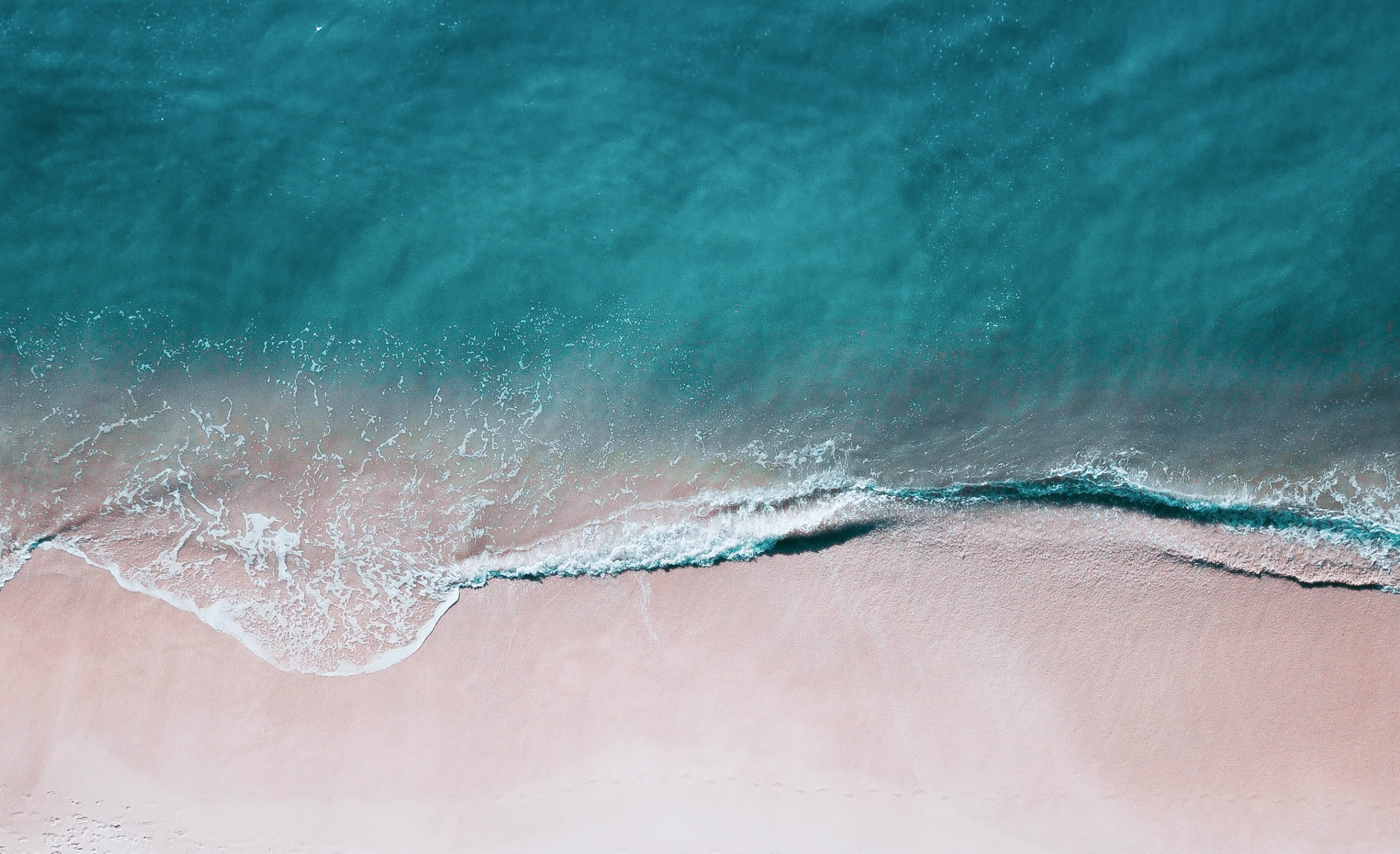 空撮で捉えられた海岸線で、透き通る青い海が砂浜に波打ち寄せている様子