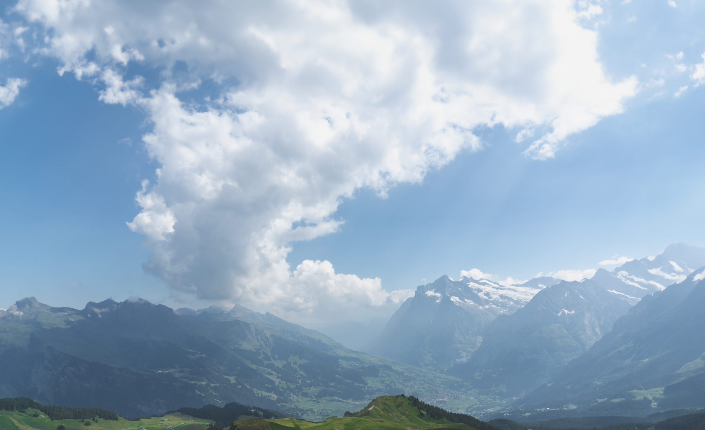黄色いレインコートを着た女性人が山の頂上に立ち、晴れた日の山々と雲の景色を眺めている