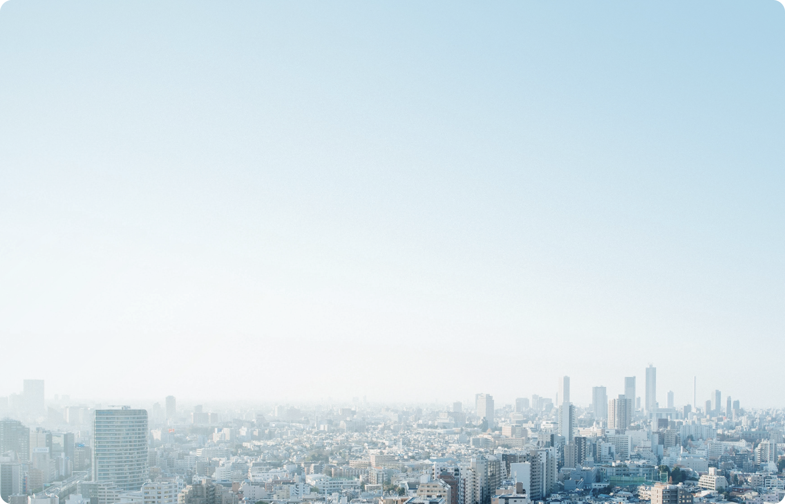 青い空の下、霞がかった都市のスカイラインが広がる様子